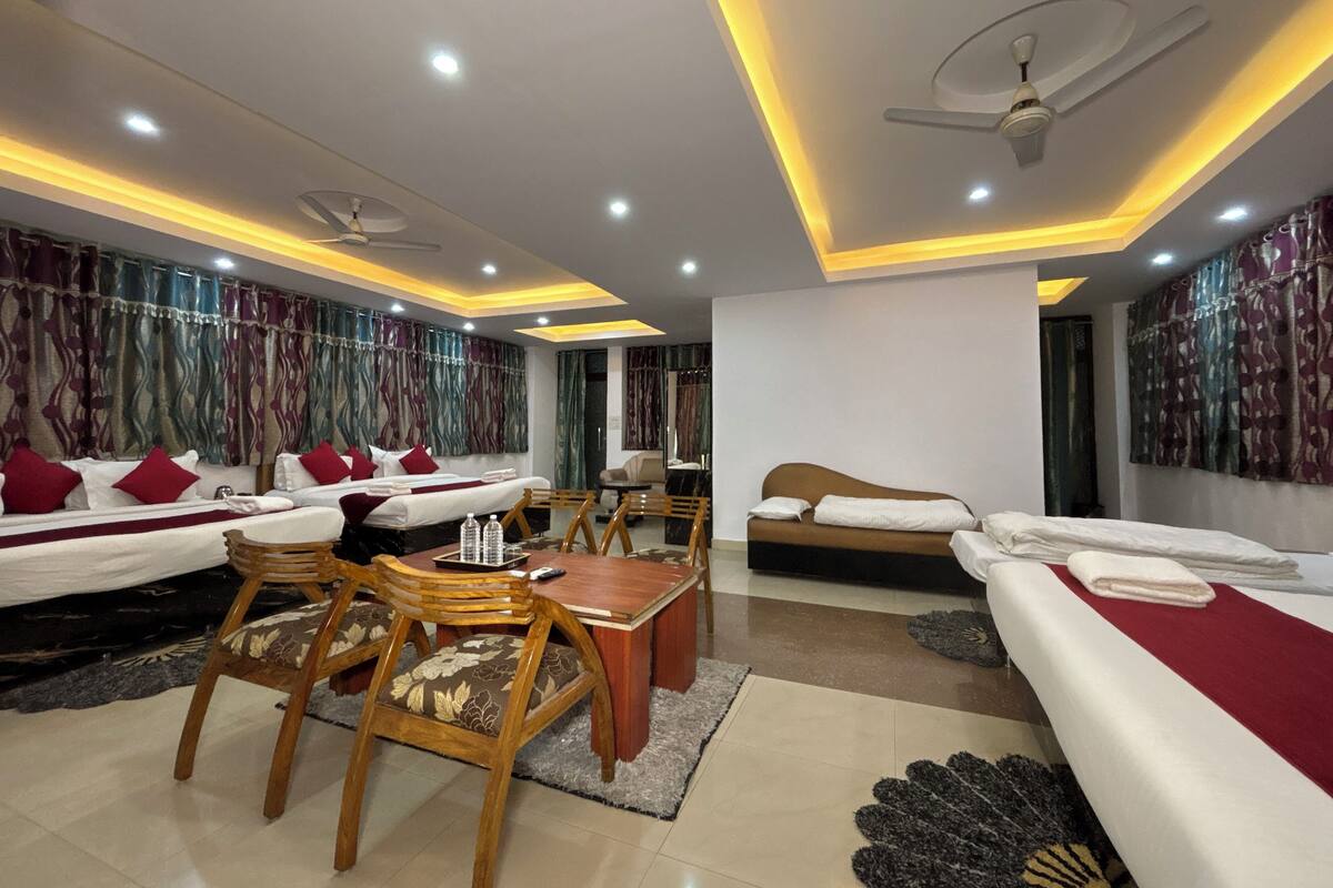 A hotel room with two beds, a dining table, chairs, a ceiling fan, and a large mirror.