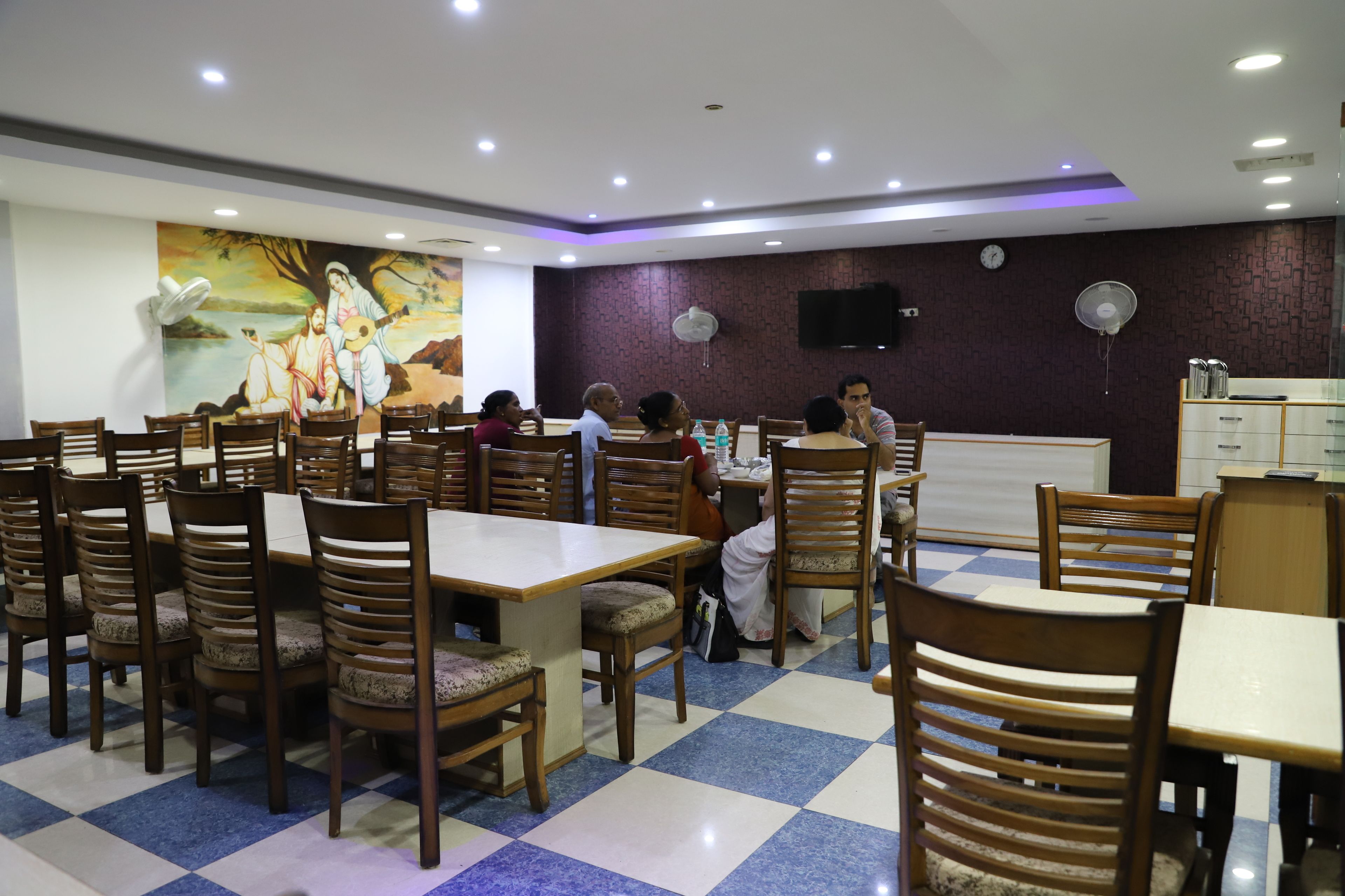 A dining area with multiple wooden tables and chairs, a checkered floor, and a mural on the wall.