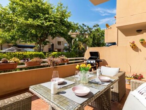 Une terrasse extérieure avec une table dressée pour le repas, entourée de plantes en pot et d’un barbecue.