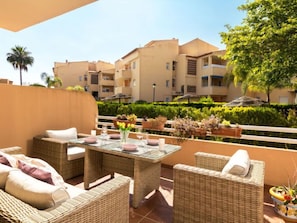 A terrace with wicker furniture, a glass-top table, and potted plants. - Reserva de Alvarito by Interhome (Marbella)