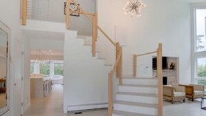 Un interior espacioso con una escalera de madera que conduce a un nivel superior, un candelabro y vistas de una zona de cocina.