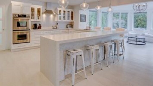 Una cocina moderna con armarios blancos, una isla grande con taburetes de bar e iluminación colgante.