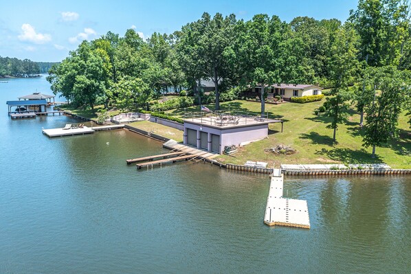 A lakeside property with a dock, a small building, and a house surrounded by trees. - Lake Sinclair Getaway + Rooftop Patio (Sparta)