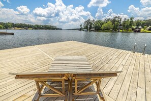 A wooden dock with a table and chairs, overlooking a calm lake with houses and trees in the background. - Lake Sinclair Getaway + Rooftop Patio (Sparta)