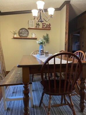 A dining area with a wooden table and chairs, a chandelier, and a wall sign that says "Eat gather around the table". - Lake Sinclair Getaway + Rooftop Patio (Sparta)