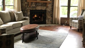 Un salon chaleureux avec une cheminée en pierre, une grande fenêtre et un fauteuil à motifs.