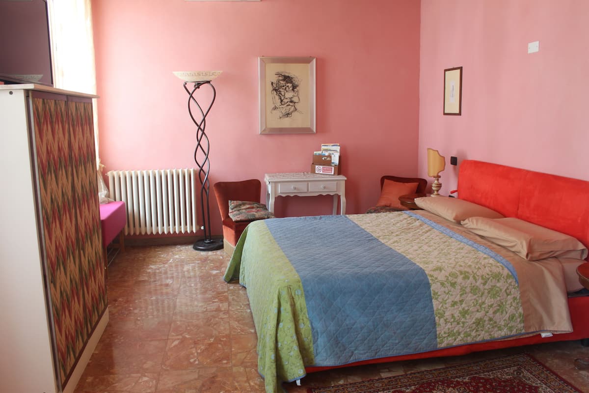 Ein Schlafzimmer mit Bett, Schreibtisch, Stuhl, Heizkörper und einem Wandbild.