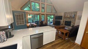 Een ruime keuken met een vaatwasser, een eethoek met een tafel en stoelen, een open haard en grote ramen met uitzicht op de omgeving.