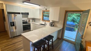 Een moderne keuken met witte kastjes, een roestvrijstalen koelkast, een ingebouwde oven en een groot eiland met barkrukken.