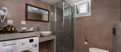A modern bathroom with a washing machine, a glass shower enclosure, a sink, and a toilet.