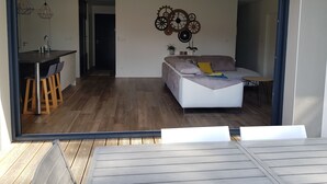 A modern living room with a sofa, a dining area with a table and chairs, and a kitchen with a sink and stools. - La Parenthèse Familiale - house with swimming pool between beach and forest (Labenne)