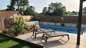 A backyard with a wooden deck, two lounge chairs, a swimming pool, and a wooden fence. - La Parenthèse Familiale - house with swimming pool between beach and forest (Labenne)