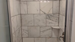 A shower with a glass door, marble tiles, and a built-in shelf. - Lake Side Room at The Copper Trout. (Bayfield)