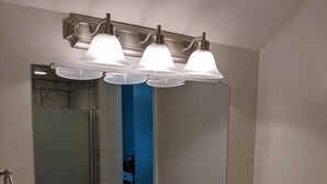 A bathroom with a large mirror, three overhead lights, a white sink, and a towel rack. - Lake Side Room at The Copper Trout. (Bayfield)