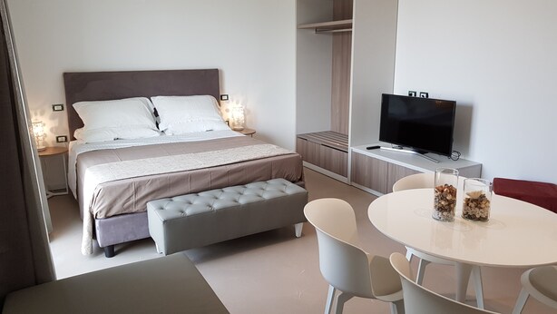 Una habitación de hotel moderna con una cama grande, televisión, zona de comedor y vestidor.
