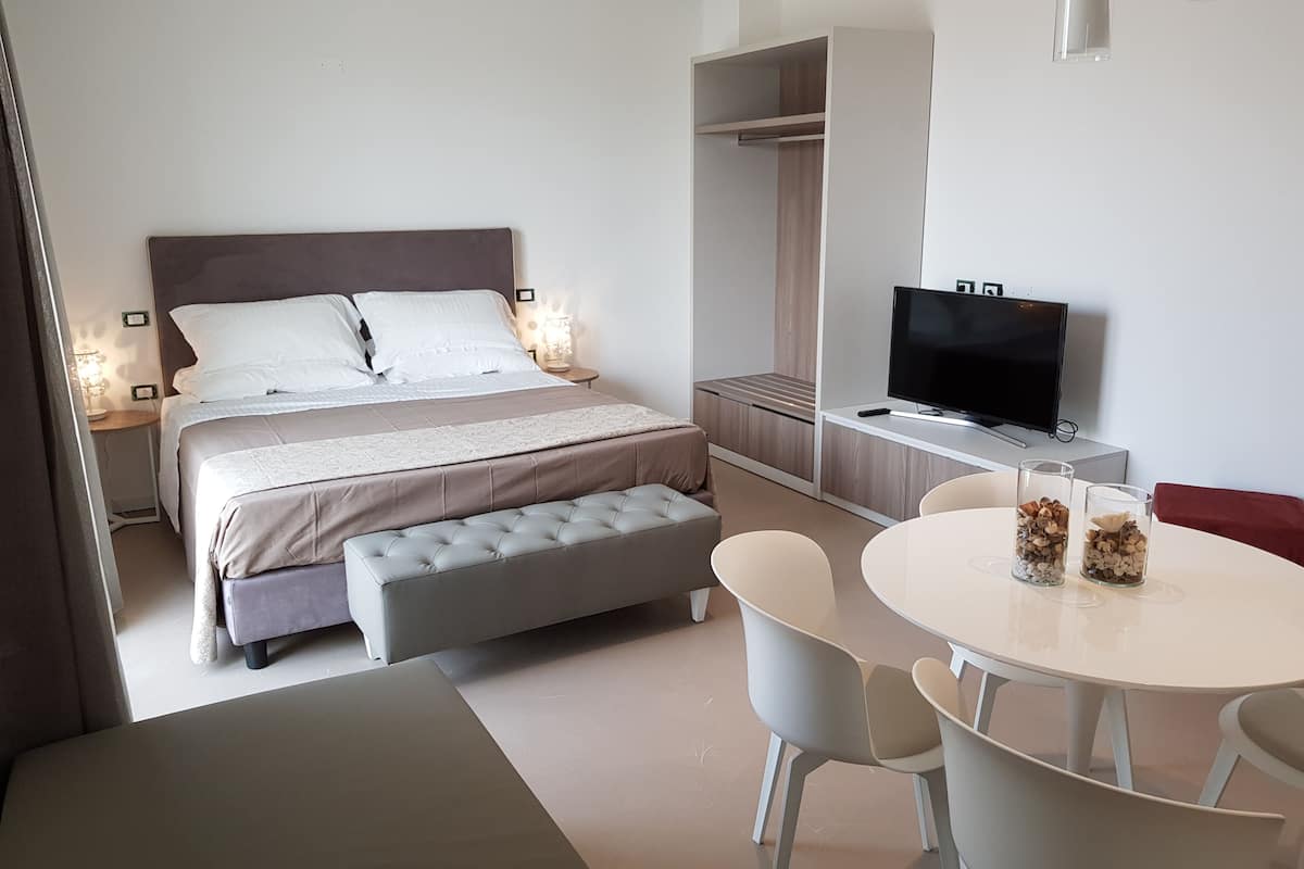 Una habitación de hotel moderna con una cama grande, televisión, zona de comedor y vestidor.