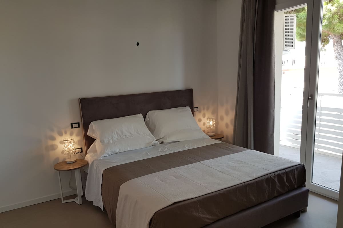 Un dormitorio con una cama grande, una mesita de noche con lámpara y vistas al exterior a través de una puerta corrediza.