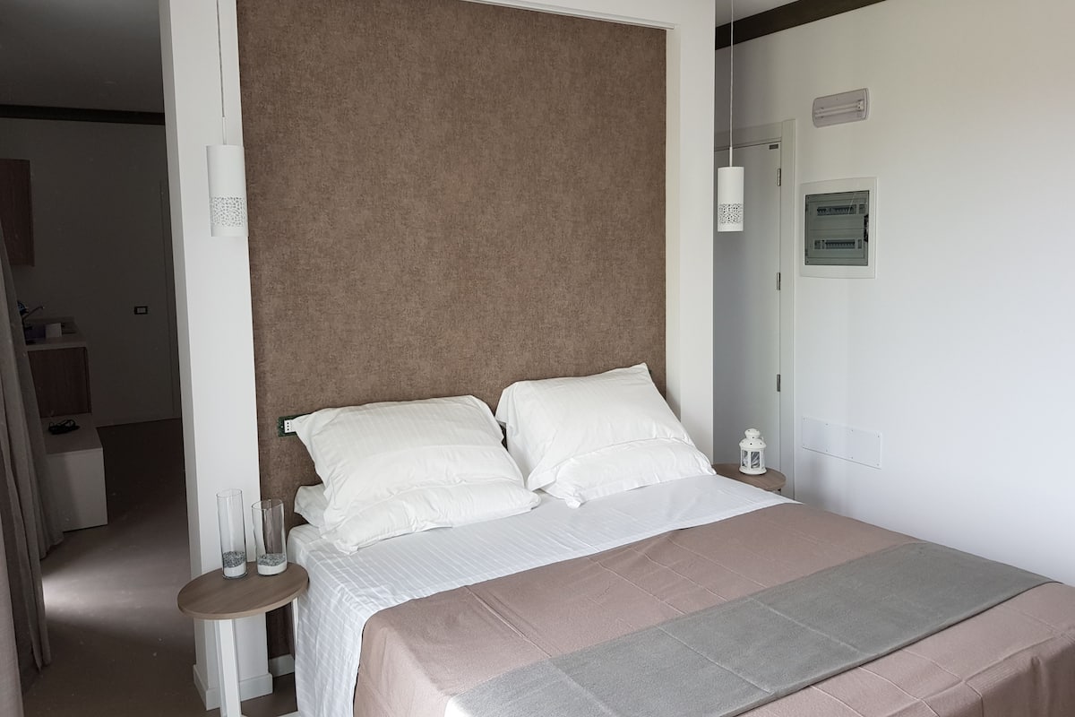 Un dormitorio con cama, mesita de noche y una lámpara de pared, además de una puerta.