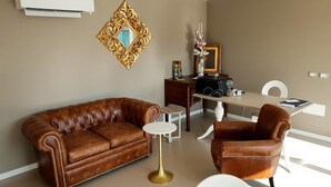Una sala de estar con un sofá de cuero marrón, un sillón a juego, una mesita redonda y una mesa de comedor con sillas.