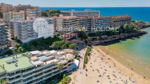 A coastal hotel with multiple floors, a beach in the foreground, and a clear view of the sea.