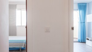 A room with a bed, a window with blinds, and a door leading to another room.
