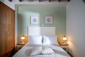 A bedroom with a bed, two bedside lamps, a wooden wardrobe, and two framed floral pictures on the wall.