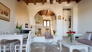 A spacious living area with a dining table, chairs, a sofa, and a kitchen in the background. - Cretan Minoan Apartments (Sitia)