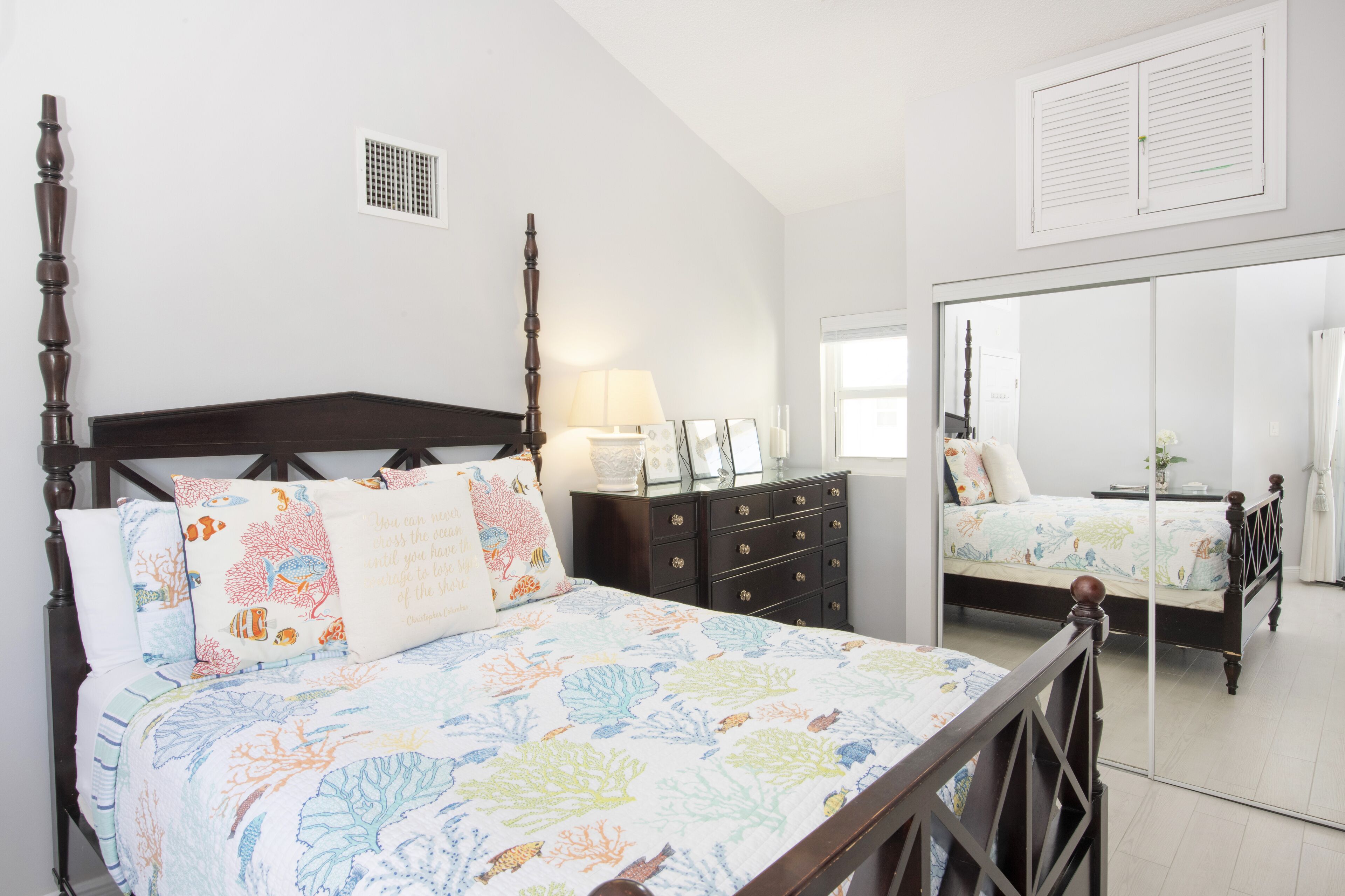 A bedroom with a four-poster bed, a dresser, a mirror, and a window.