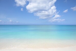 Uma praia com águas turquesa cristalinas e uma faixa de areia dourada sob um céu azul com nuvens.