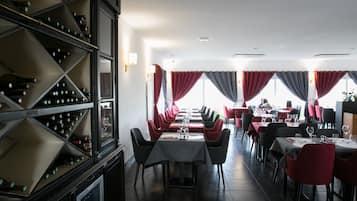 Un restaurante con un amplio comedor, sillas negras y rojas, y una estantería con botellas de vino.