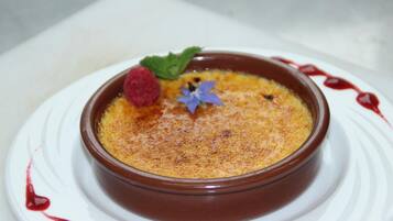 A dessert in a brown ramekin on a white plate with a raspberry and mint garnish.