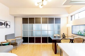 A modern living room with a dining area, a large window with frosted glass panels, and a flat-screen TV mounted on the wall.