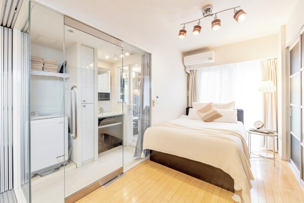A modern bedroom with a glass closet, a bed with a white duvet, and a bedside table with a clock.