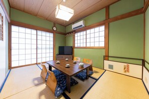 A tatami mat room with a wooden table, chairs, and a television.