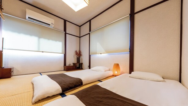 Habitació d'hotel amb dos llits, sòl de tatami, paret d'estil japonès tradicional i aire condicionat.