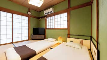 A traditional Japanese-style room with tatami flooring, two beds with pillows, a television, and an air conditioning unit.