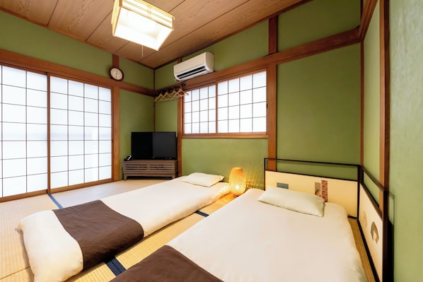 A traditional Japanese-style room with tatami flooring, two beds with pillows, a television, and an air conditioning unit. - USJ / Quiet Private Japanese Traditional House, close to Osaka fish market! (Osaka)