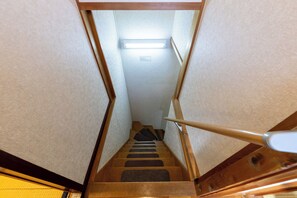 A narrow stairway with wooden steps and a handrail, leading to a landing with a light fixture.