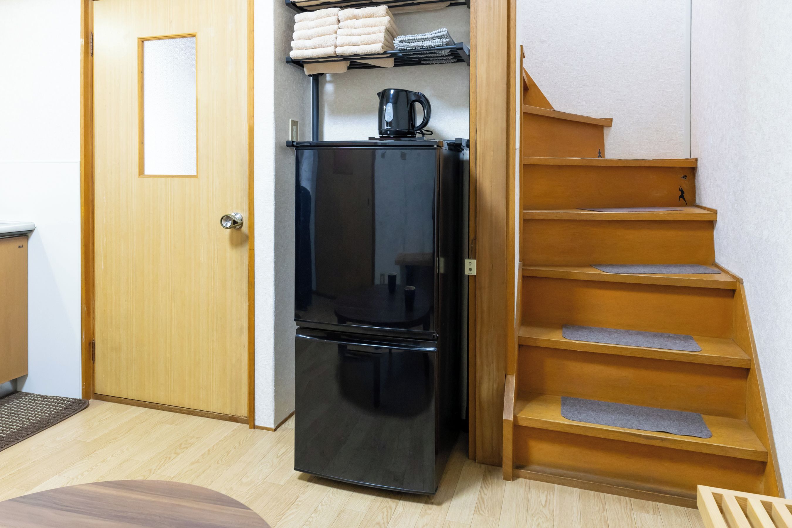 A compact kitchen with a black refrigerator, a wooden staircase, and a door with a frosted glass panel.