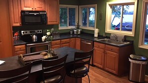 A kitchen with wooden cabinets, a microwave, a stove, a sink, and a dining area with chairs and a table. - Waterfront Home with large pond (Belgrade)