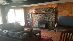 A living room with a stone fireplace, wooden walls, a sofa, a TV, and a wooden chair. - Waterfront Home with large pond (Belgrade)