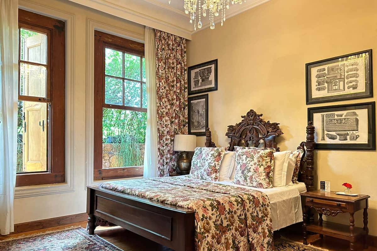 Ein Schlafzimmer mit einem großen Bett, blumigen Vorhängen, einem Kronleuchter und gerahmten Bildern an der Wand.