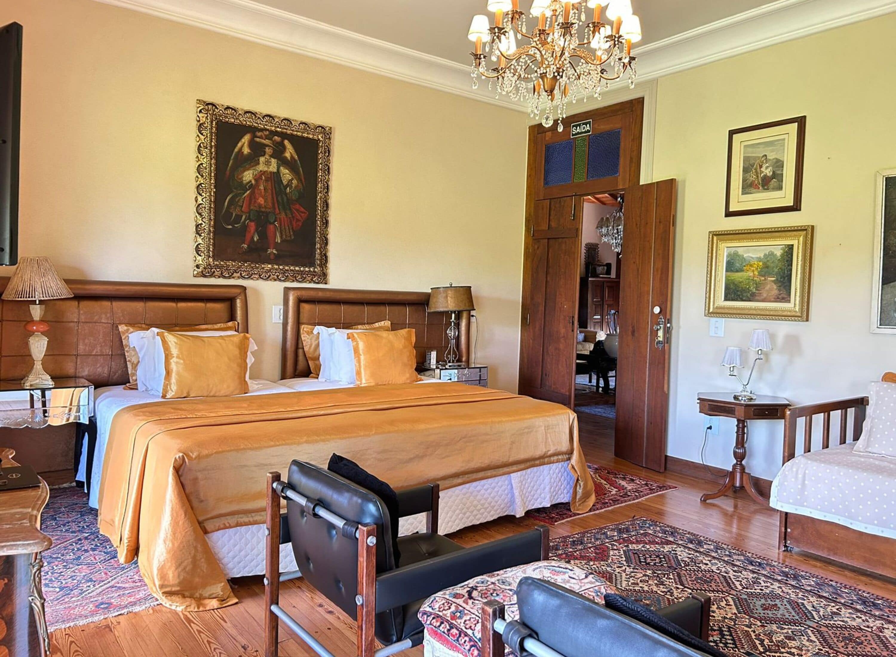 Une chambre d’hôtel spacieuse, dotée d’un grand lit, d’un coin salon avec un fauteuil, d’un bureau et d’un lustre.