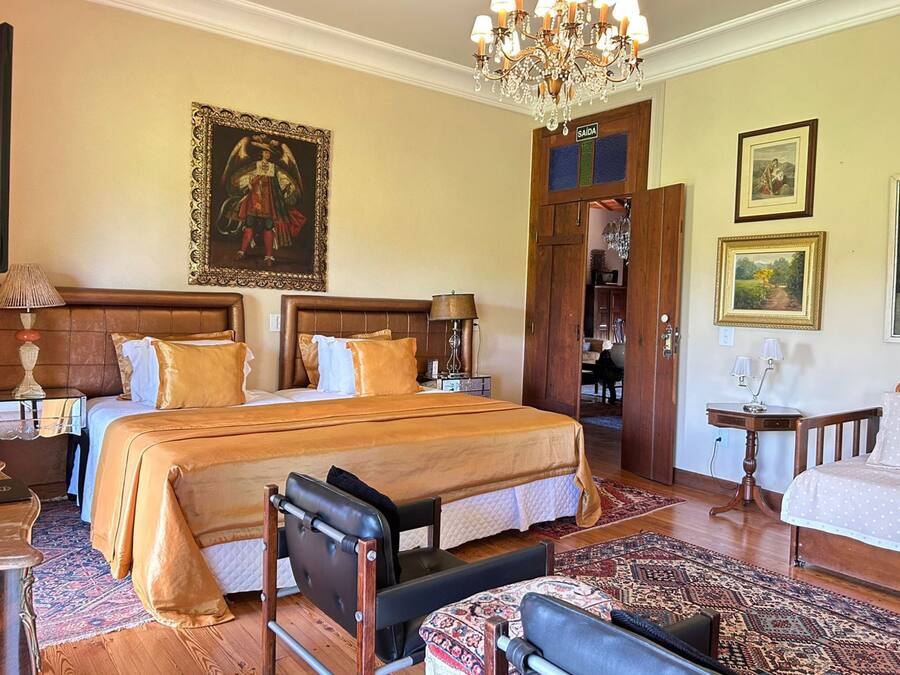 Une chambre d’hôtel spacieuse, dotée d’un grand lit, d’un coin salon avec un fauteuil, d’un bureau et d’un lustre.