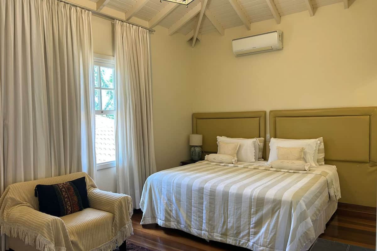 Ein Schlafzimmer mit Bett, Stuhl, einem fensterbepflanzten Fenster, einer Klimaanlage und Holzboden.