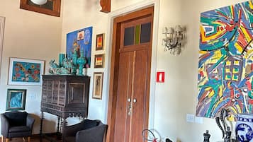 A room with a wooden door, a fireplace, two black chairs, a colorful abstract painting, and a chandelier.