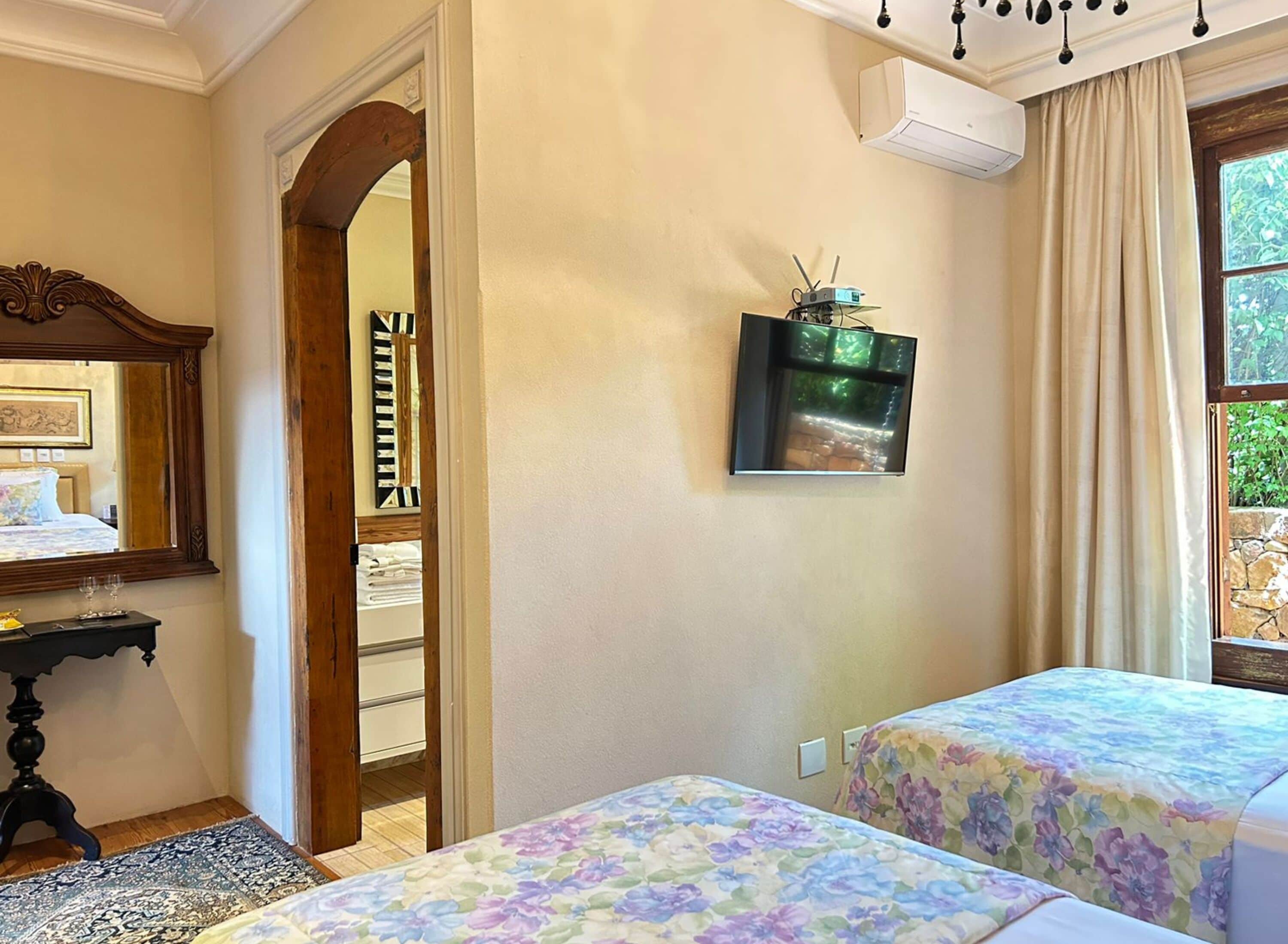 A hotel room with two beds, a wooden door, a mirror, a small table, and a wall-mounted air conditioner.