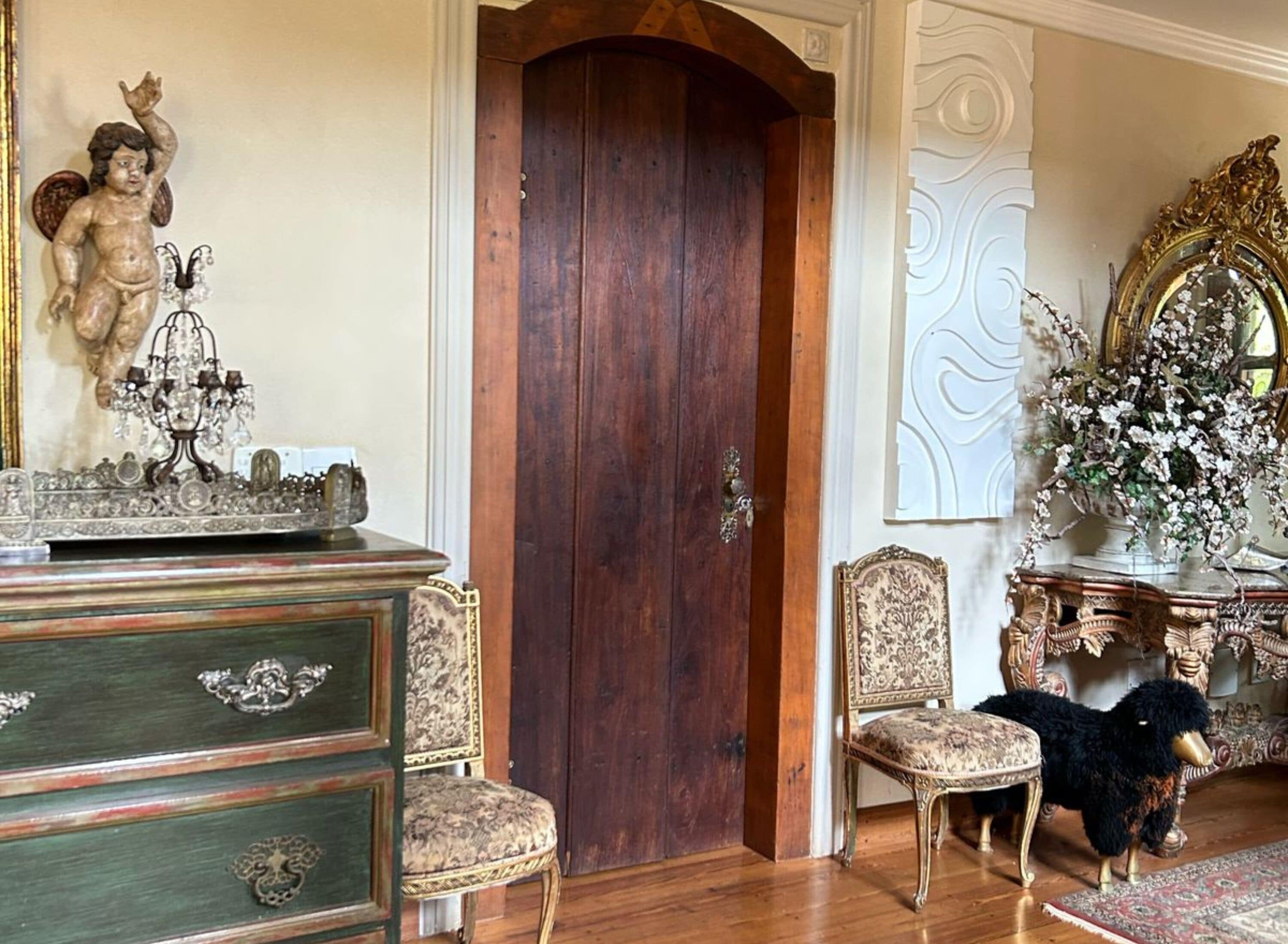 A room with a wooden door, a chandelier, ornate furniture, and a decorative mirror.
