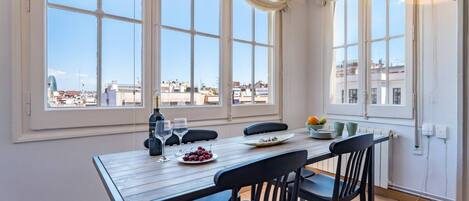 A dining area with a table set for two, a bottle of wine, and a bowl of fruit.