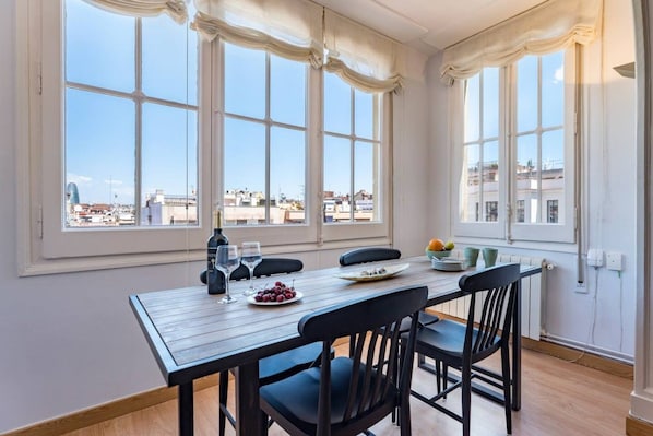 A dining area with a table set for two, a bottle of wine, and a bowl of fruit.